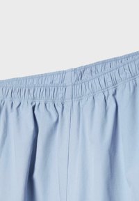 Shorts à taille élastique bleu clair avec tissu froncé et détails de couture visibles sur un fond textile lisse.