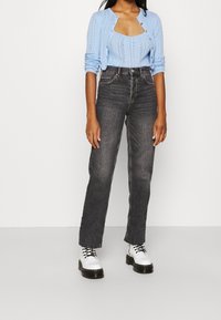 Cárdigan de punto azul claro sobre una camiseta sin mangas a juego, combinado con unos vaqueros de pierna recta de cintura alta en negro y calzado blanco.