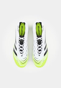 White soccer cleats with black accents, textured surface, and bright green sole. Features include laces and 'Predator' branding.
