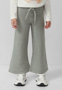 Graue, flauschige, weit geschnittene Hosen mit einem Kordelzugbund. Kombiniert mit weißen und silbernen Sneakern. Weiche Textur mit lockerer Passform.