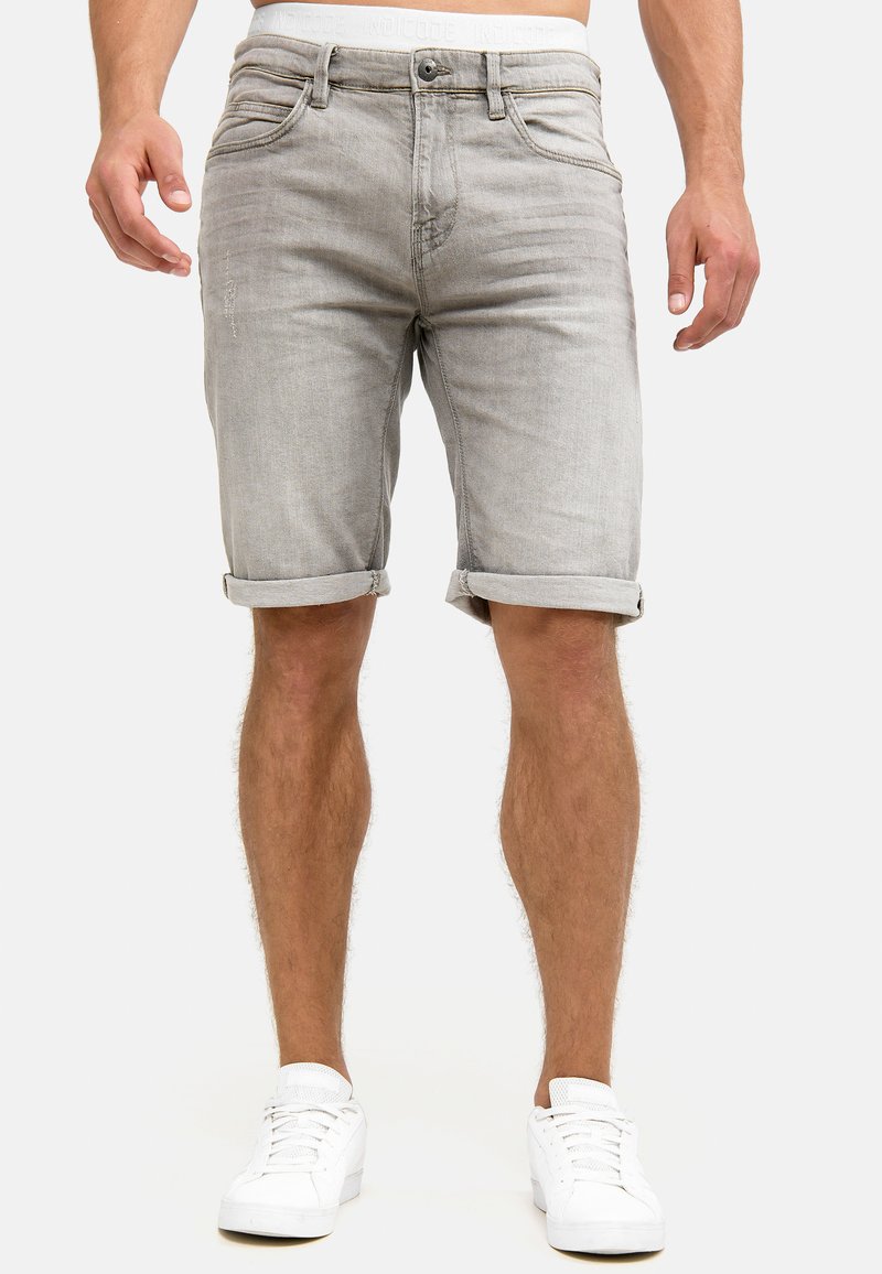 Shorts en denim gris clair avec des ourlets retroussés, design à cinq poches et détails de coutures subtils, accompagnés de baskets blanches.