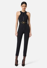 Tutina nera con una silhouette aderente, caratterizzata da un collo alto, chiusura a zip frontale e una cintura decorata con dettagli dorati. Tessuto liscio con cuciture sartoriali.