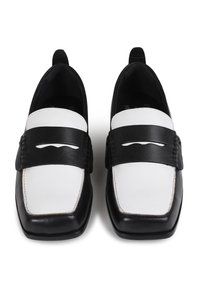 Mocasines en blanco y negro hechos de cuero, con una punta cuadrada plana, una amplia correa negra con detalles troquelados y costuras decorativas.