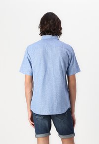 Chemise à manches courtes, bleu clair avec un motif discret, col boutonnière et ourlet arrondi, associée à un short en denim foncé.