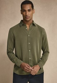 Vaaleanvihreä napitettavat paita pehmeästä kankaasta; siinä on kaulus, pitkät hihat ja suora helma, jossa on hienovaraisia ompeluyksityiskohtia.