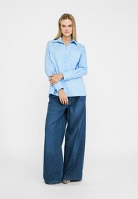 Lichtblauwe, lange mouwen knoopshirt met verticale stikdetails, gecombineerd met wijde, donkere denim jeans. Glad stoftextuur.