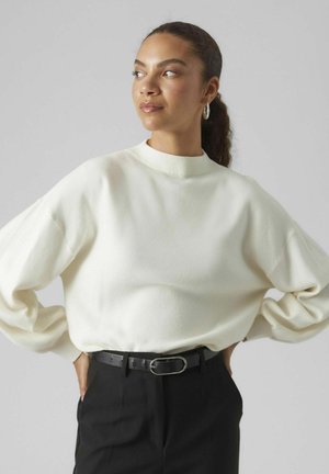 Cream-colored sweater with a high mock neck and oversized sleeves, paired with black tailored pants and a black belt featuring an oval buckle.