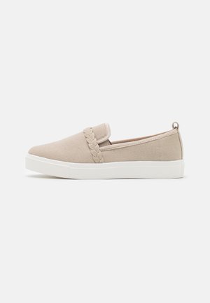 Baskets slip-on beiges avec semelle en caoutchouc blanche et détail tressé sur le dessus, présentées sur un fond clair et simple.