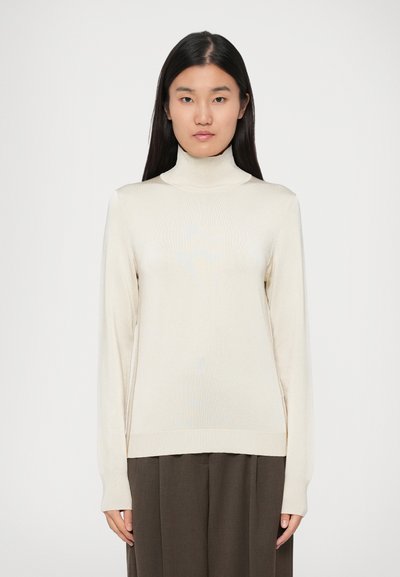 Pull en col roulé crème, tissu tricot léger, manches longues, design ajusté, poignets et ourlet côtelés, assorti à un pantalon marron foncé.