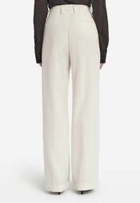 Weite Hosen aus strukturiertem, weißem Cord. Hohe Taille mit Gürtelschlaufen und Taschen. Die Rückansicht zeigt klare Linien und eine maßgeschneiderte Passform.