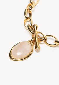 Złota bransoletka z łańcuszkiem, ozdobiona różowym kamieniem w kształcie gładkiego owalu, wyposażona w zapięcie na przekładkę dla pewnego mocowania.