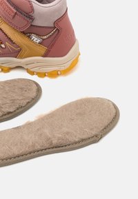 Chaussure de cheville rose et grise avec semelle jaune et tige en textile, à côté d'une semelle intérieure en laine beige avec une surface texturée et un bord cousu.