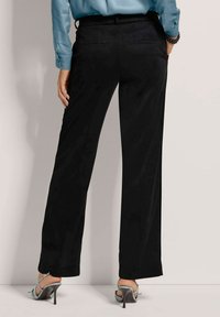 Zwarte, wijde broek met een gladde stof, met een gedefinieerde tailleband en twee achterzakken. Gemaakt met een lichtblauw top en haksandalen.