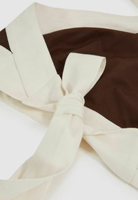 Brūns audums ar krēmkrāsas lentu, kas rotāta ar elegantu mezglu. Materiāls izskatās gluds ar nelielu spīdumu.