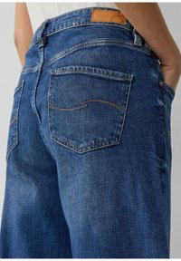 Jean en denim bleu taille haute avec une coupe décontractée, des coutures orange et deux poches arrière avec des coutures arrondies et une étiquette en cuir.