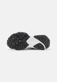 Semelle de chaussure de sport en noir et blanc avec caoutchouc texturé pour une meilleure adhérence, présentant divers motifs de semelle et des éléments de conception flexibles.