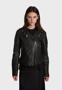 Veste de moto en cuir noir avec un design ajusté, fermeture éclair frontale asymétrique, accents matelassés aux épaules et détails en métal argenté.