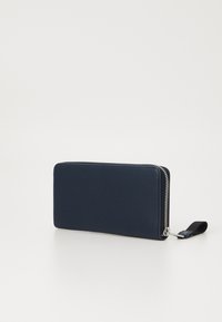 Portafoglio blu navy con una texture liscia, forma rettangolare e chiusura con zipper argentata. Dotato di una tracolla per un trasporto facile.