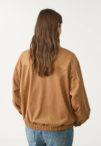Chaqueta marrón de gran tamaño con una textura suave, cintura elástica y hombros caídos, combinada con jeans de color azul claro.