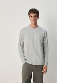 Graues Langarmshirt mit Rundhalsausschnitt aus weichem Stoff, mit schlichtem Design und Rippbündchen, kombiniert mit dunkelgrauer Cargo-Hose.