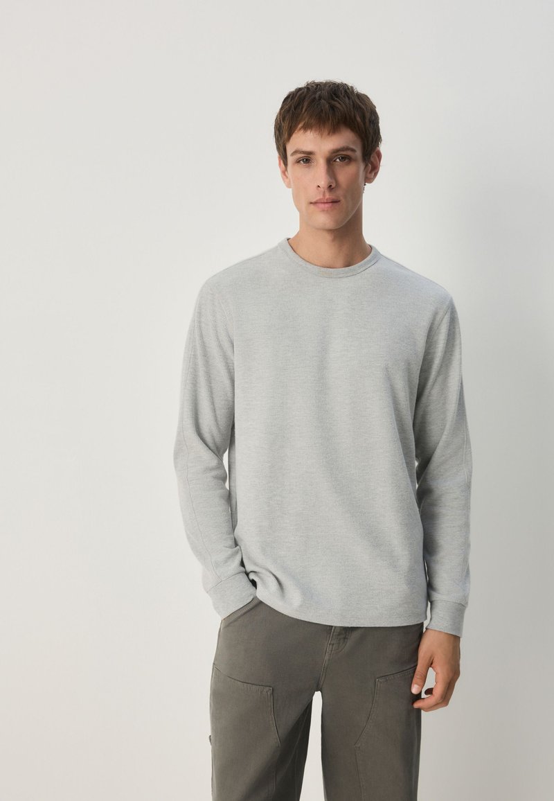 Gray long-sleeve crew neck shirt made of soft fabric, featuring a simple design and ribbed cuffs, paired with dark gray cargo pants.