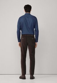 Camisa de cuadros azul de botones con mangas largas, combinada con pantalones marrones y zapatos oscuros y lisos. Tejido texturizado y diseño limpio.