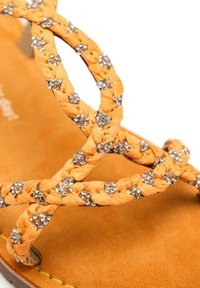 Cinghie intrecciate arancioni decorate con strass argento, su una soletta in suede marrone. Cuciture dettagliate visibili.