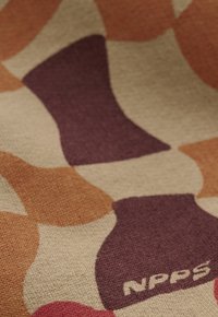 Nahaufnahme von Strickstoff mit abstrakten Formen in Beige, Braun, Orange und Rot, mit zwei stilisierten Socken und dem Text "NPPS" auf einer Socke.