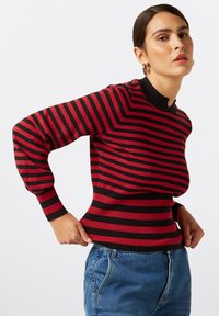 Gestreifter Pullover in Rot und Schwarz mit geripptem Textur, tailliertem Schnitt und hohem Kragen. Lange Ärmel mit leichtem Puffdetail.