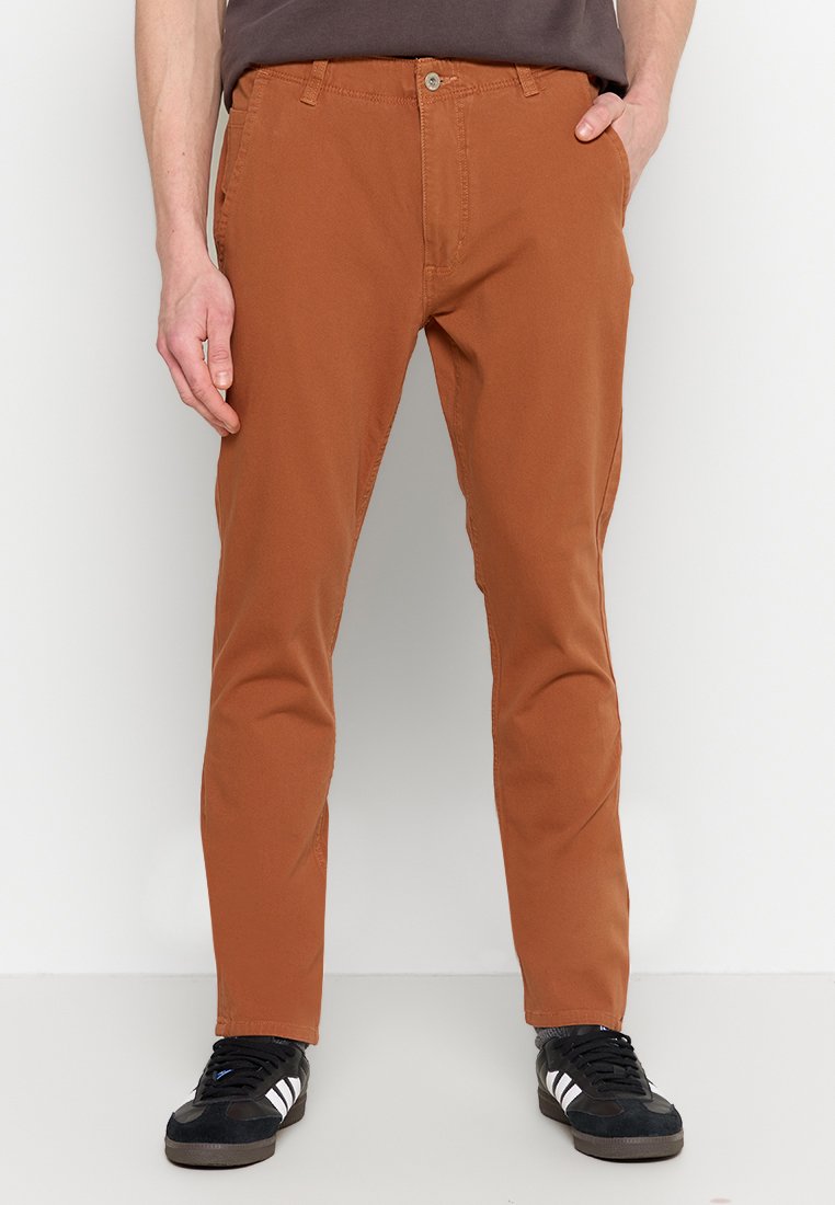 Pantalons en coton orange avec une coupe slim, dotés de poches latérales et arrière, d'une fermeture à bouton standard, portés avec des baskets noires.