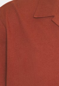 Červená texturovaná tkanina se strukturovaným límcem a výrazným tkaním. Materiál vypadá odolně a je mírně drsný.