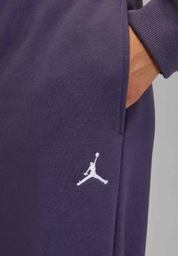 Paarse sweatbroek met geribbelde manchetten en zijzak. Heeft een wit Jordan-logo geborduurd aan de onderkant rechts.