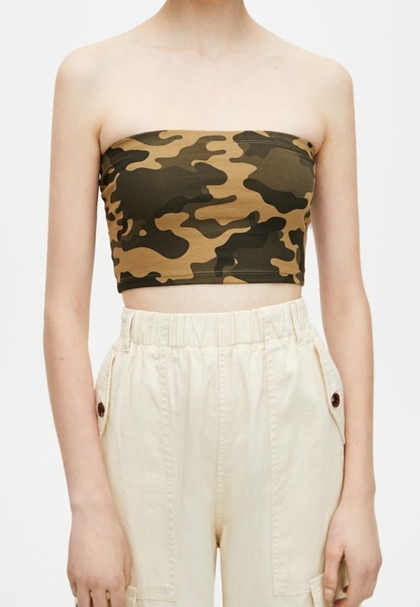 Personne portant un crop top bustier camouflage marron et vert et un pantalon beige taille haute avec poches latérales boutonnées.
