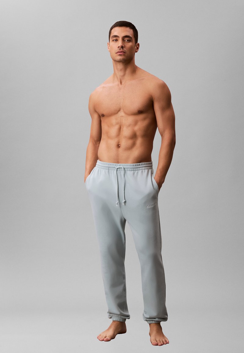 Jasnoszare spodnie dresowe z elastycznym pasem i sznurkiem do regulacji. Miękki materiał, ściągacze przy kostkach oraz boczne kieszenie. Prosty design bez wzorów.