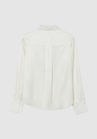 Chemise blanche à manches longues avec yoke arrière et pli central, poignets boutonnés et ourlet arrondi, présentée sur un fond uni.
