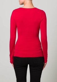Rode lange mouwen top met een ronde hals, fitted ontwerp, geribbelde textuur en knoopaccenten op de mouwen, gecombineerd met zwarte broek.