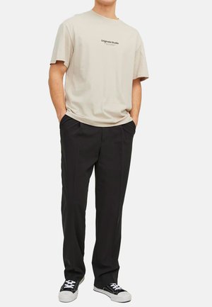 Beige T-shirt with a printed logo, black tailored pants, and black and white sneakers. Casual fit, short sleeves, and a round neckline.