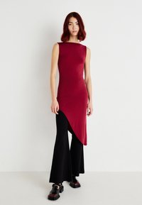 Top bordeaux sem mangas com uma bainha assimétrica, combinado com calças pretas de perna larga e sapatos pretos. Textura suave com detalhes mínimos.