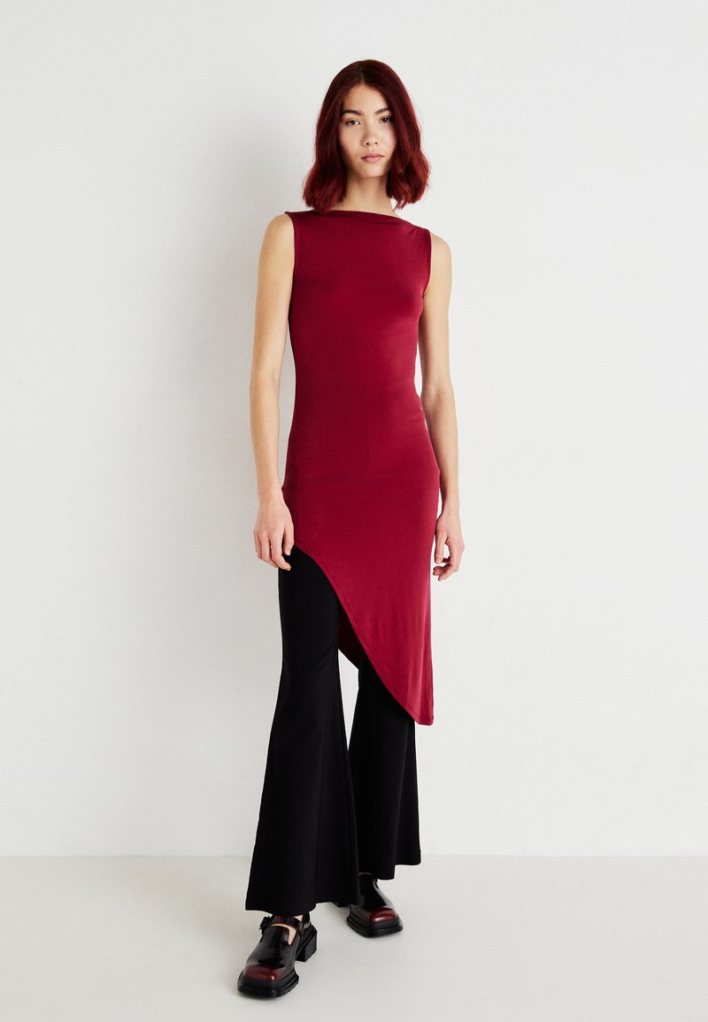 Top bordeaux sem mangas com uma bainha assimétrica, combinado com calças pretas de perna larga e sapatos pretos. Textura suave com detalhes mínimos.