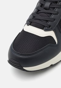 Zapatillas navy con parte superior texturizada, detalles de cuero suave, una media suela blanca contrastante y un diseño de cordones estándar.