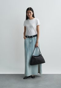 Λευκή φανέλα με στρογγυλή λαιμόκοψη, μακριά φούστα από ανοιχτό μπλε τζιν, μαύρη ζώνη, πλεκτή μαύρη τσάντα και μαύρα επίπεδα παπούτσια. Απλή, καθημερινή εμφάνιση.