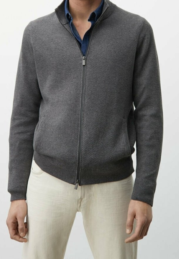 Graue Strickjacke mit Reißverschluss und strukturiertem Muster, gerippte Bündchen und Saum, getragen über einem blauen Hemd, kombiniert mit hellen Hosen.