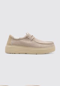 Zapatillas de color beige sin cordones con parte superior de tejido texturizado, detalles de costura y suela gruesa beige. Presentan una puntera redondeada y un diseño ligero.