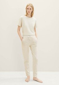 T-shirt beige clair à manches courtes associé à un pantalon de jogging beige à motifs avec un design géométrique et un cordon de serrage, porté pieds nus.