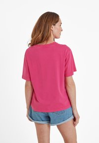 Pink cotton t-shirt with short sleeves, round neck, and a relaxed fit, paired with denim shorts, viewed from the back.