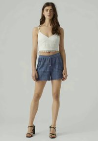 White cropped top with lace detailing paired with blue patterned shorts featuring a drawstring waist. Model wearing black high heels.