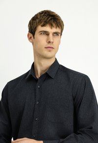 Ciemnoszara koszula na guziki wykonana z teksturowanej tkaniny, z ostrokątnym kołnierzykiem, kieszenią na przodzie i subtelnym wzorem na całej powierzchni.