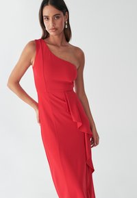 Vestido rojo de un solo hombro, confeccionado con una tela ligera y detalle de volantes laterales. Textura suave, corsé ajustado, diseño fluido y caída elegante.