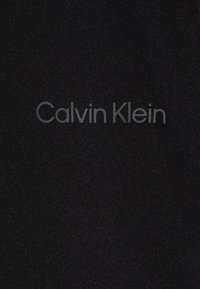 Tessuto nero con una texture liscia, con il logo "Calvin Klein" stampato in un grigio sottile. Design semplice e minimalista senza ulteriori motivi.