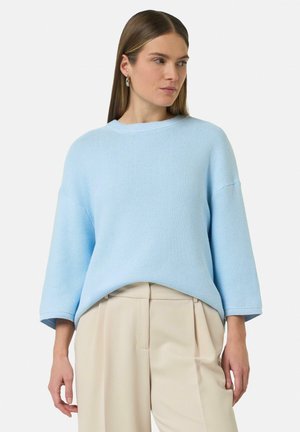 Light blue knitted sweater with a round neckline, dropped shoulders, and ribbed cuffs, paired with beige pleated trousers.